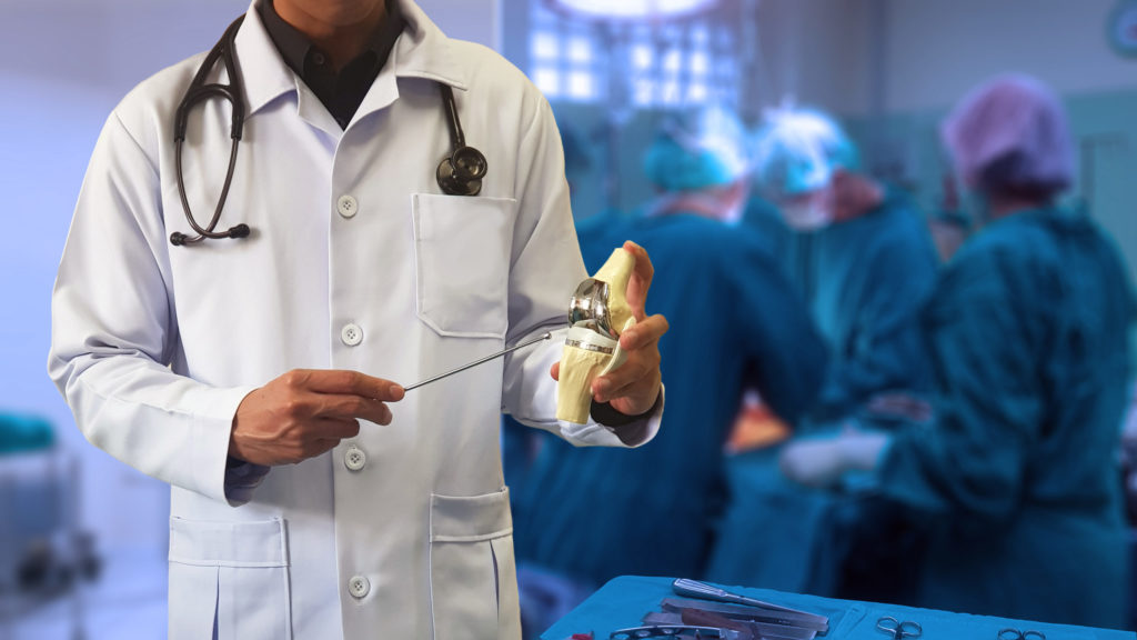 Orthopedic surgeon holds a prosthetic knee joint before a surgical procedure.